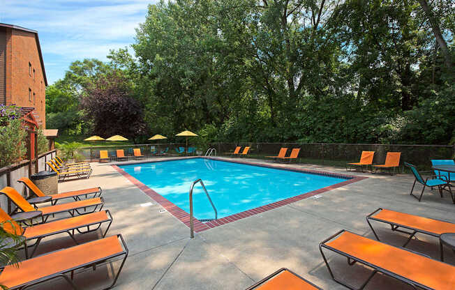 A pool surrounded by orange lounge chairs and umbrellas.