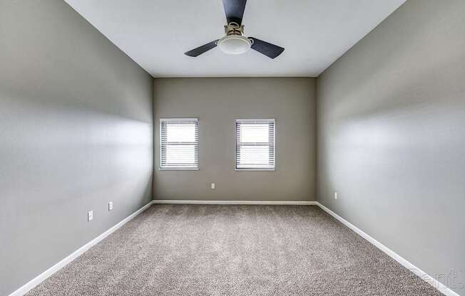 A room with a ceiling fan and two windows.