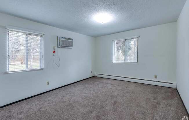 A room with a carpeted floor, a window with blinds, and a wall-mounted air conditioner unit.