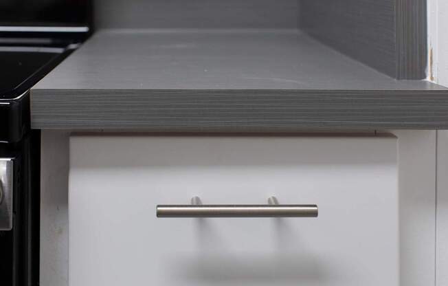 A white drawer with a silver handle is in a kitchen.