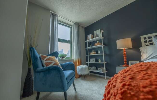 a bedroom with a blue chair and orange bedspread
