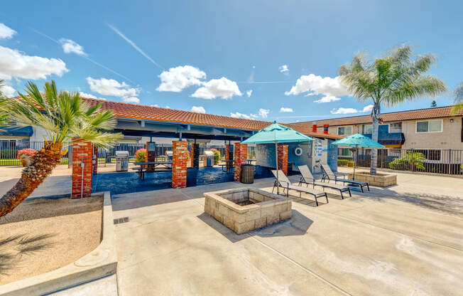 a patio with a fire pit and umbrellas in front of a building