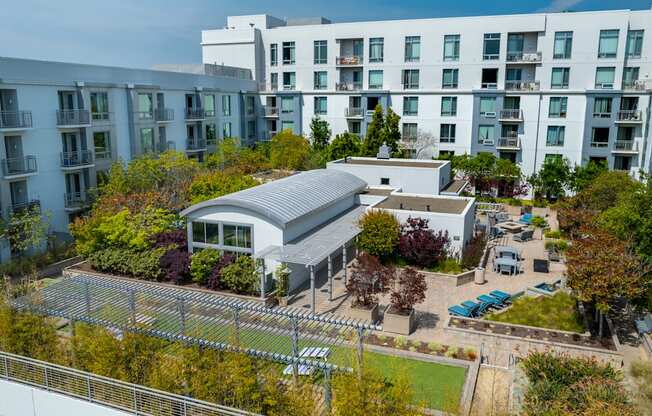 A modern building with a grey roof is surrounded by trees and other buildings.