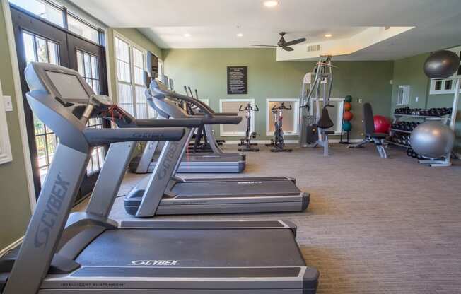 a gym with treadmills and other exercise equipment in a building with windows