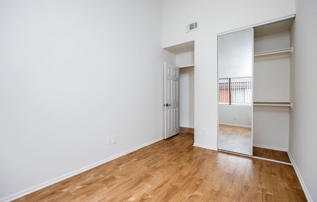 an empty room with wood flooring and a mirrored closet