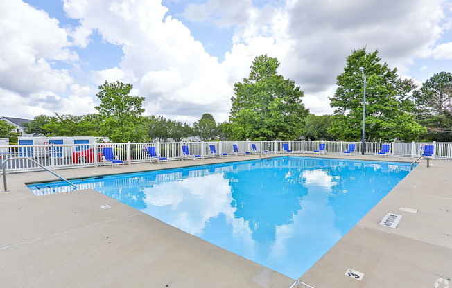 A large outdoor swimming pool surrounded by trees and a fence.