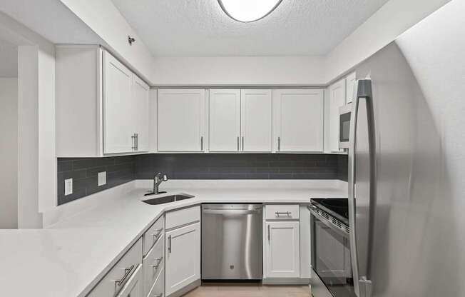 A kitchen with white cabinets and a black backsplash.