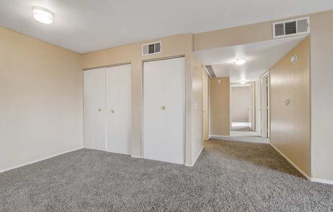 A room with carpeted floor and white walls with three closets.
