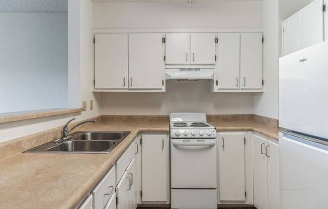 an empty kitchen with white cabinets and appliances and a sink