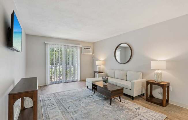 A living room with a white couch, a wooden coffee table, and a flat-screen TV mounted on the wall.
