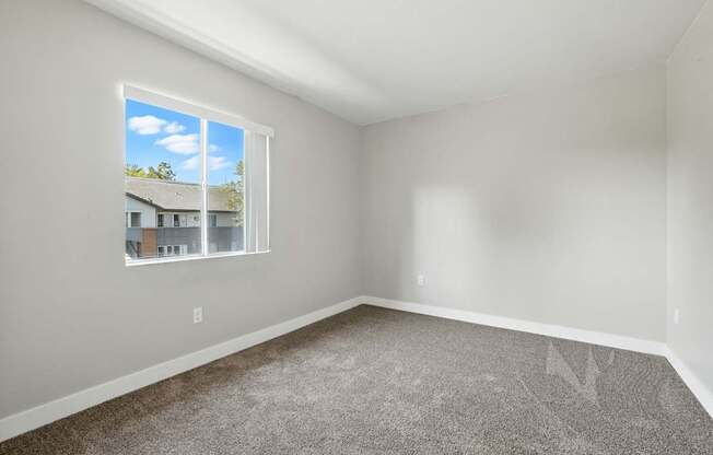 A room with a carpeted floor and a window showing a house and sky.