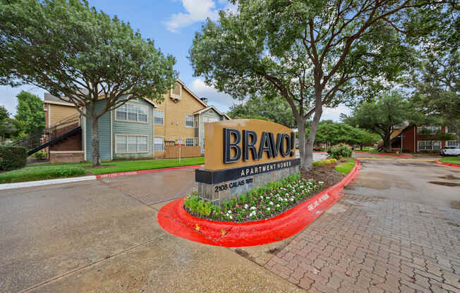 A sign for Bravo Apartments is in front of some trees and buildings.