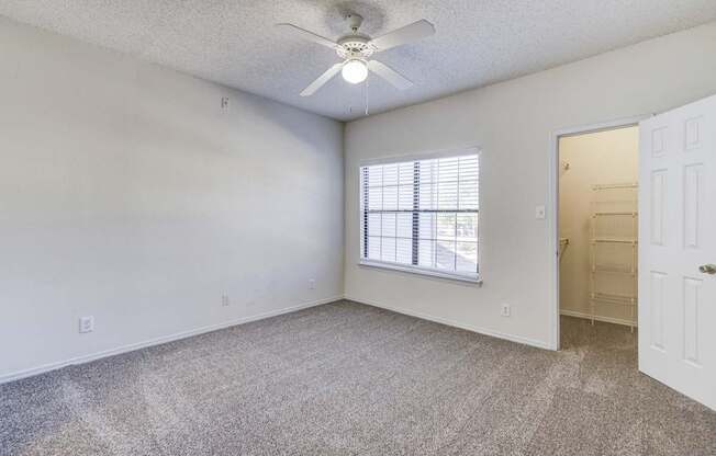 Bedroom at Saxony at Chase Oaks Apartments in Dallas, TX, with white walls, neutral carpeting, a ceiling fan, and a walk-in closet.