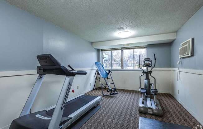 A room with a treadmill, exercise bike, and a vacuum cleaner.