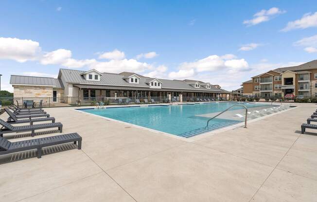 A large swimming pool with lounge chairs and a building in the background.