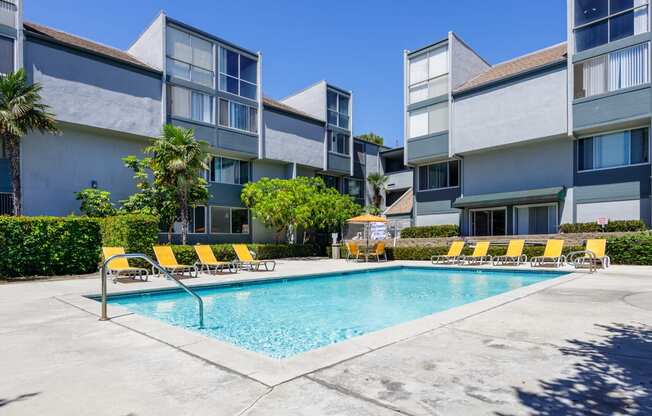 a swimming pool with yellow chairs in front of an apartment building