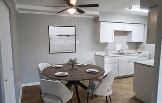 A dining room with a table set for two and a kitchen in the background.