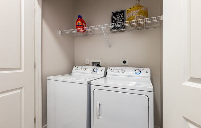 a washer and dryer in a small laundry room with a shelf above them
