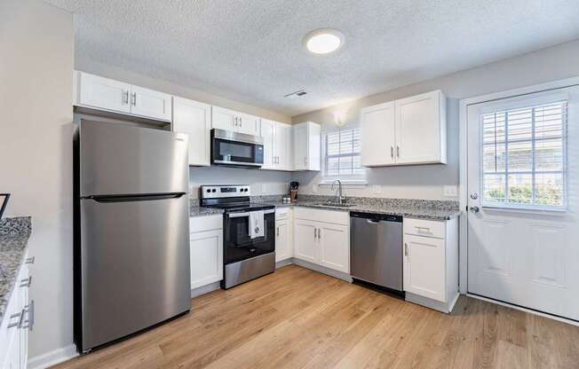 A kitchen with a refrigerator, microwave, oven, and sink.