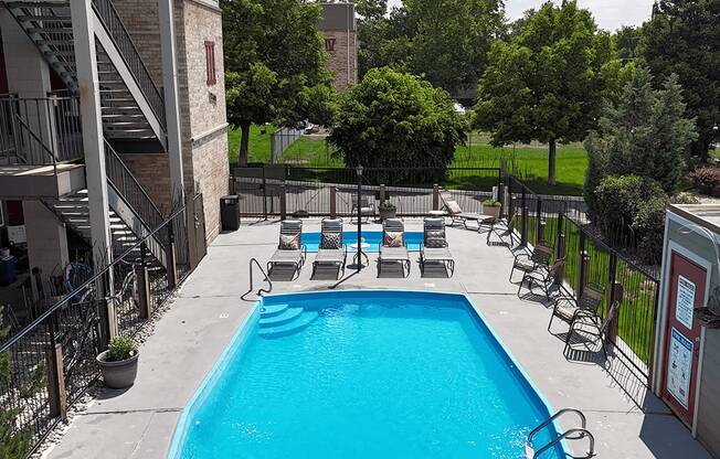 A pool surrounded by chairs and trees.