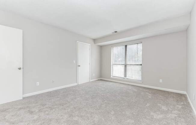 A room with a carpeted floor and a window with blinds.