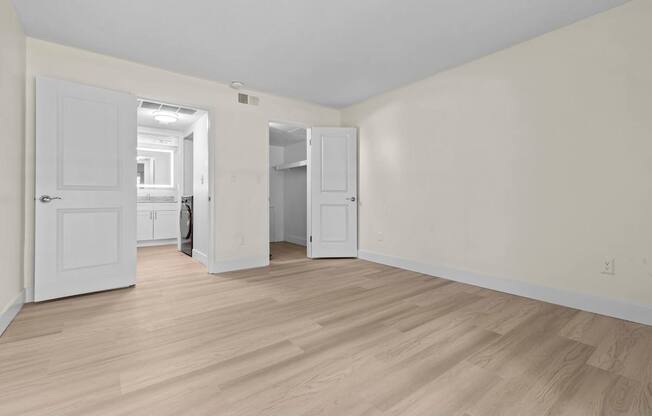 A room with white walls and wooden flooring with a door and a cabinet.