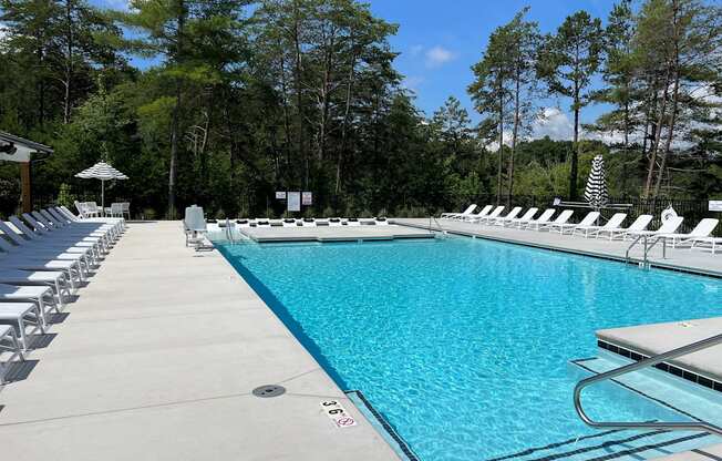 a swimming pool with chaise lounge chairs and trees in the background