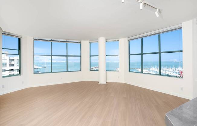 A large empty room with wooden floors and large windows overlooking a city.