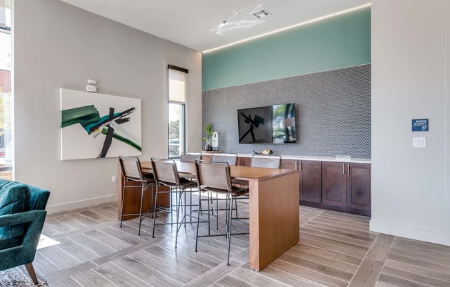 A room with a wooden table and chairs and a painting on the wall.