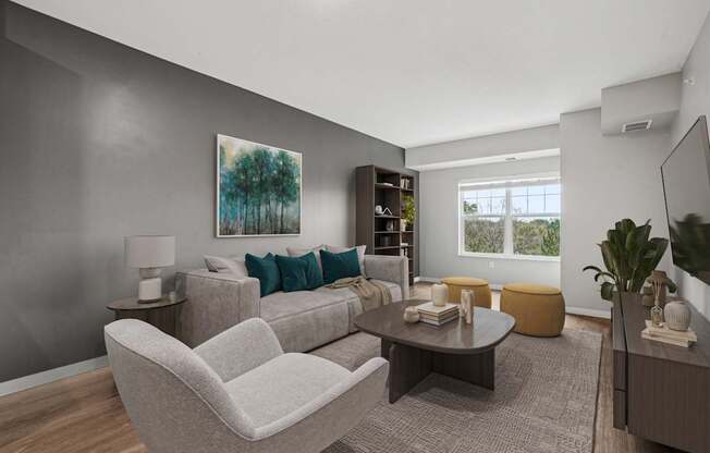 A living room with a grey couch, a grey armchair, a coffee table, a lamp, a book, a plant, and a painting on the wall.