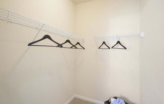 A room with a white wall and a shelf with clothes hanging on it.