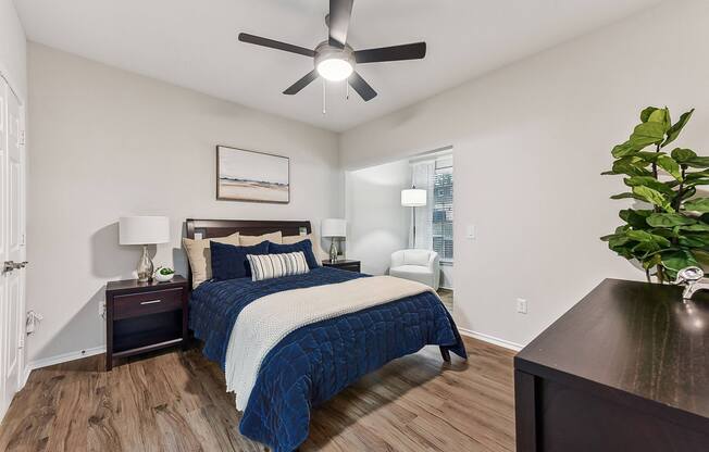 A bedroom with a bed, nightstand, and a plant.