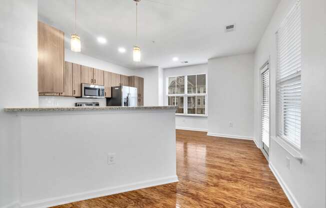 an empty living room with a kitchen and a hard wood floor