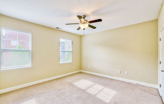 large bedroom with two windows and ceiling fan an light