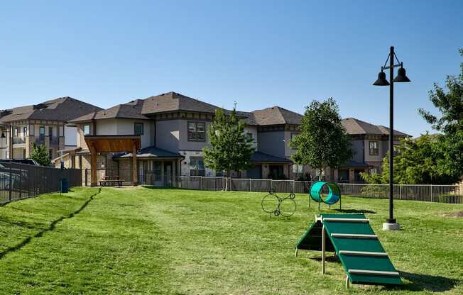 A playground with a slide, swings, and a seesaw in front of a row of houses.