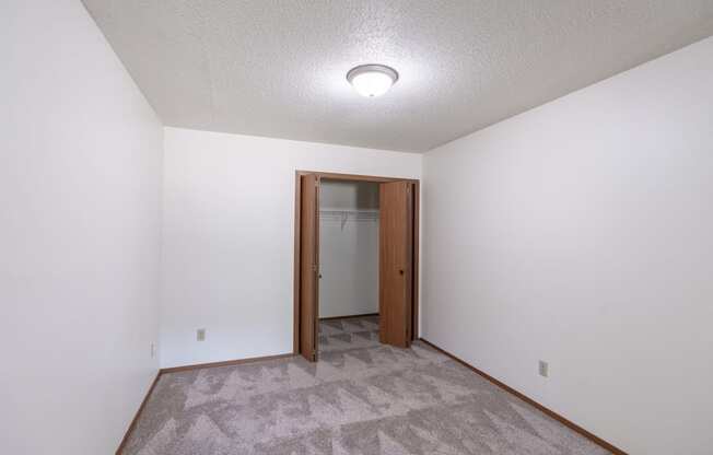 a room with a carpeted floor and a door to a closet. Fargo, ND Rosegate Apartments