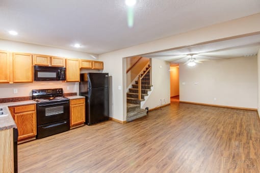 the kitchen and living room of an empty house with wood flooring and black appliances