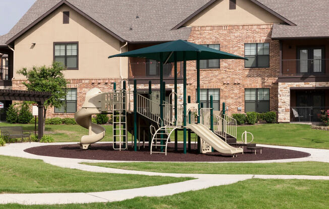 A playground with a green umbrella and a slide.