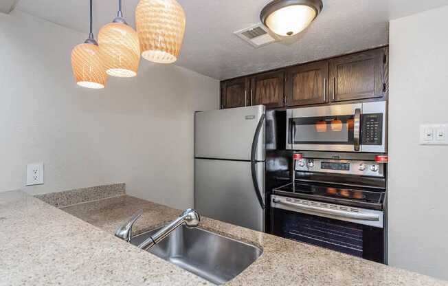 A kitchen with a stainless steel refrigerator and oven, a sink, and three hanging lights.