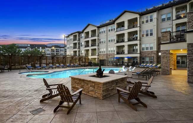 an outdoor pool with chairs and a fire pit at night