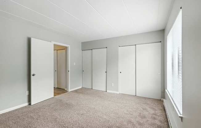 A room with white walls and a carpeted floor with four closets.