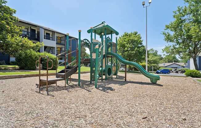 A playground with a green slide and a brown bench.