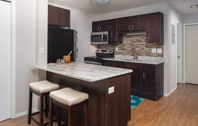 A kitchen with a black fridge, brown cabinets, and a marble countertop.at Prosper West, Minnesota