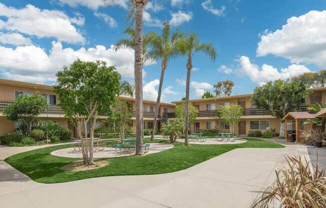 a courtyard with palm trees and a sidewalk in front of a building at Villa La Paz Apartments, California, 90706