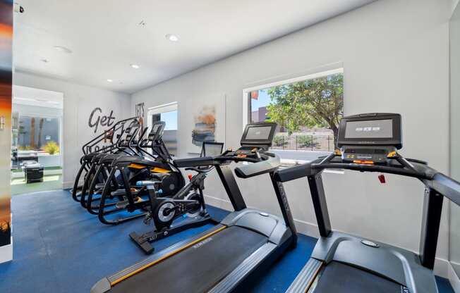 a gym with various cardio equipment on the floor and a window