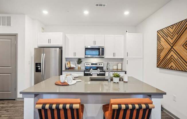 an open kitchen with an island with three chairs and a stainless steel refrigerator and microwave