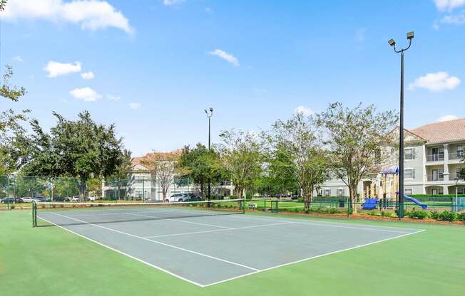 A tennis court surrounded by trees and a building in the background.