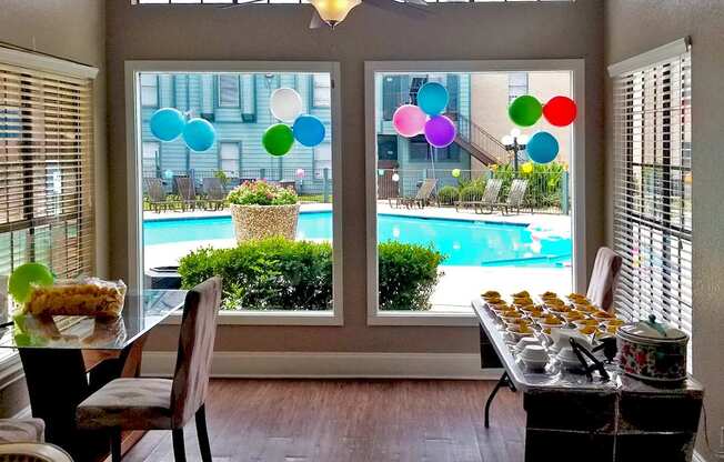 A table with food on it is in front of a window with a view of a pool.