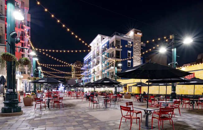 a plaza at night with red chairs and umbrellas and street lights