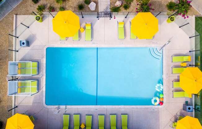 Aerial view of Fusion Las Vegas apartments community pool surrounded by lime green lounge chairs and cabanas with bright yellow umbrellas.